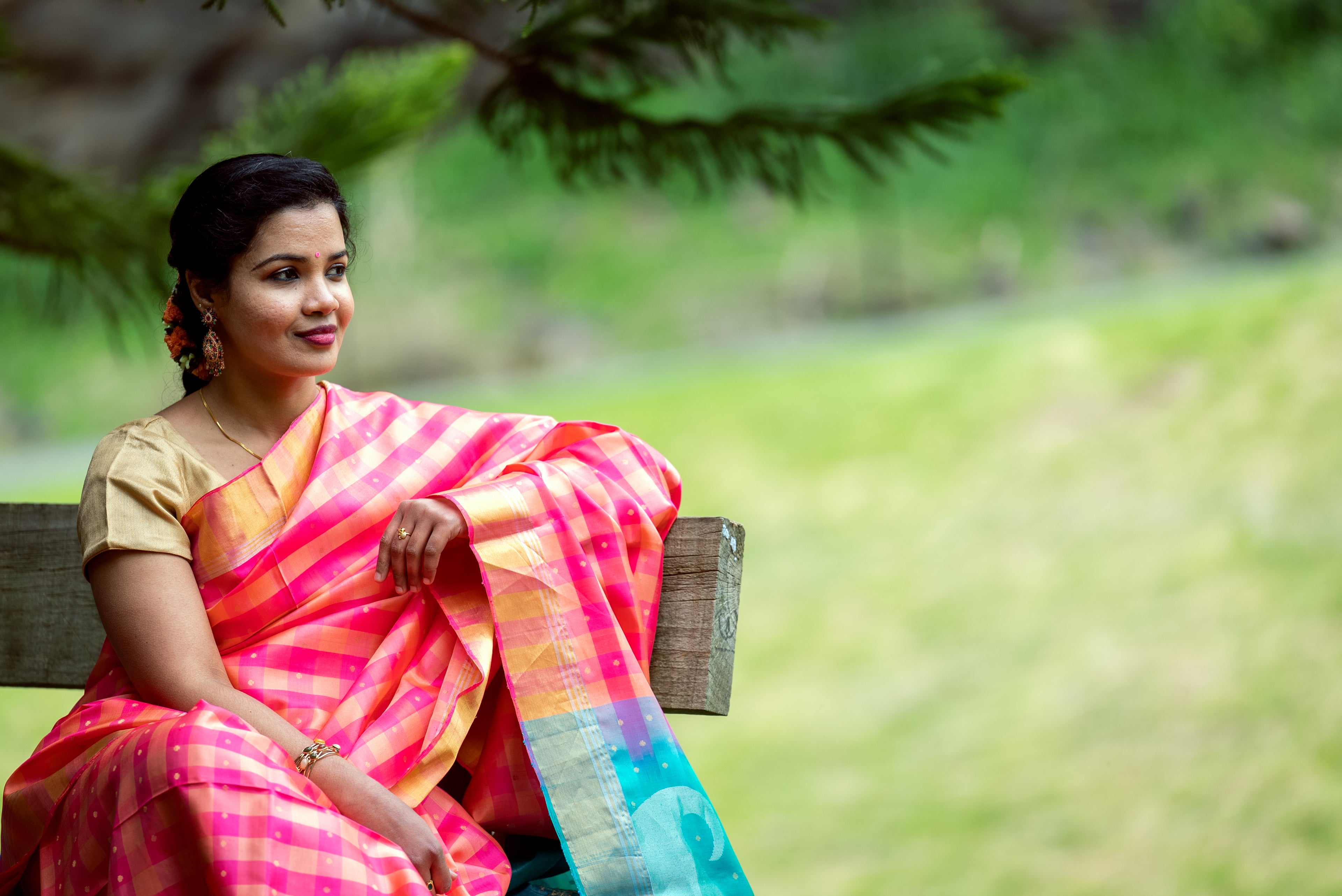 Person sitting on a bench wearing pink and teal saree.