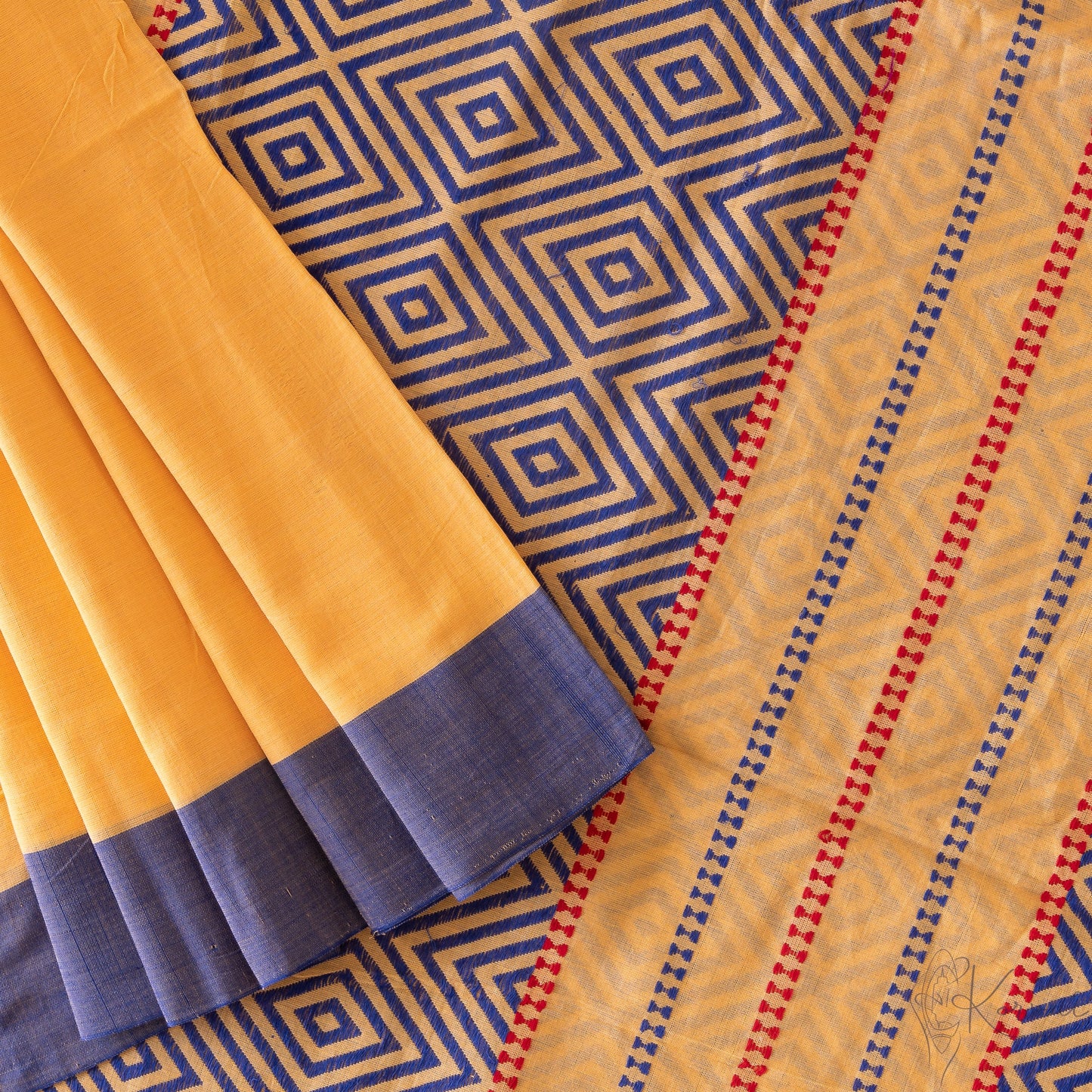 Top view of yellow kadhi cotton saree showing the pallu that has dark blue diamond motifs and some pleats.