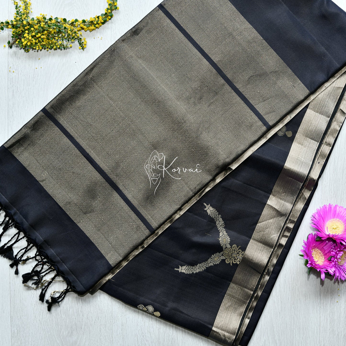 Top view of black soft silk saree featuring necklace and jhumka motifs in gold and silver.