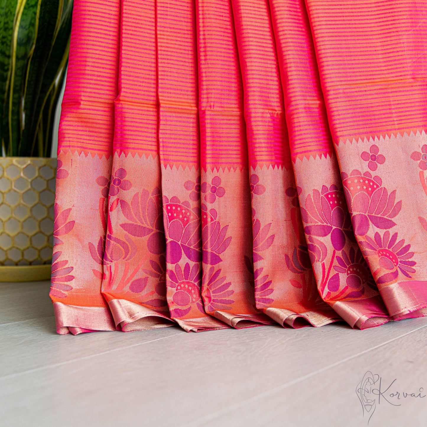 Pleated view of hot pink soft silk saree with purple and pink coloured lotus motifs in the border.