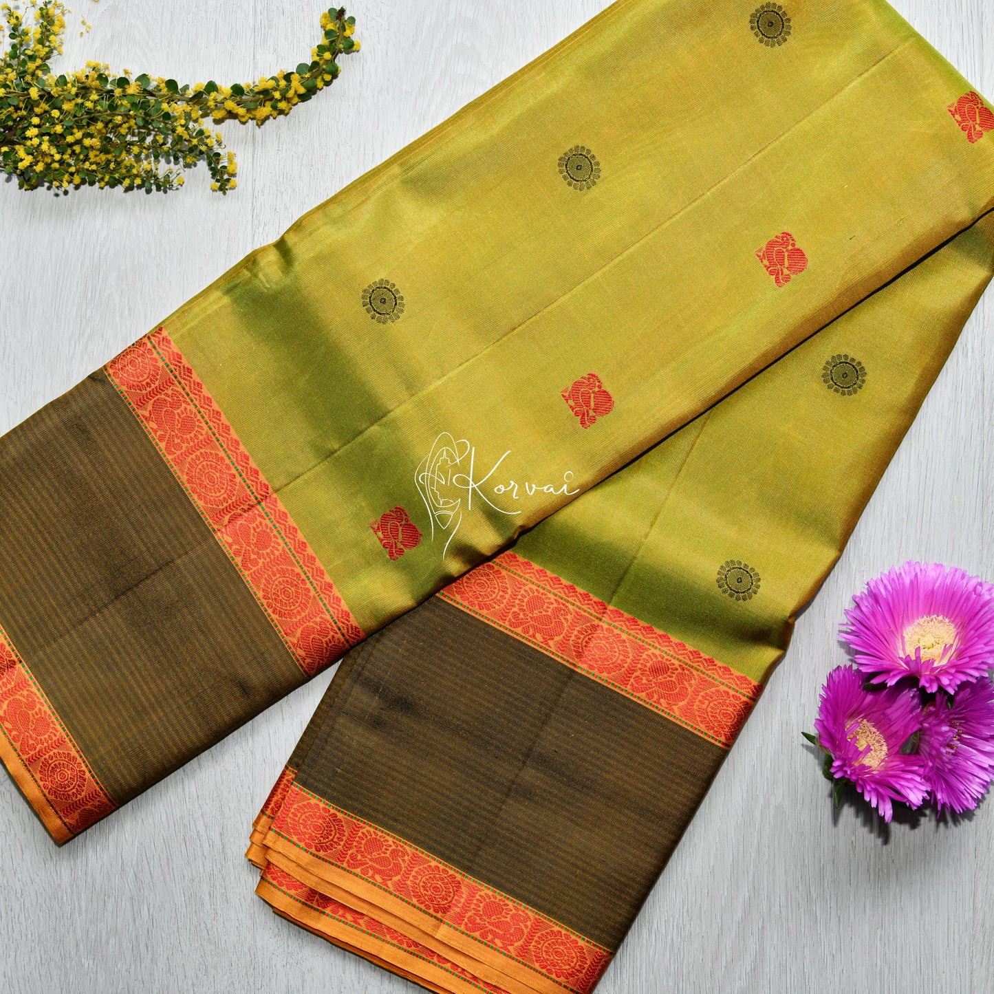 Top view of green soft silk saree with double border in orange featuring peacock and wheel motifs.