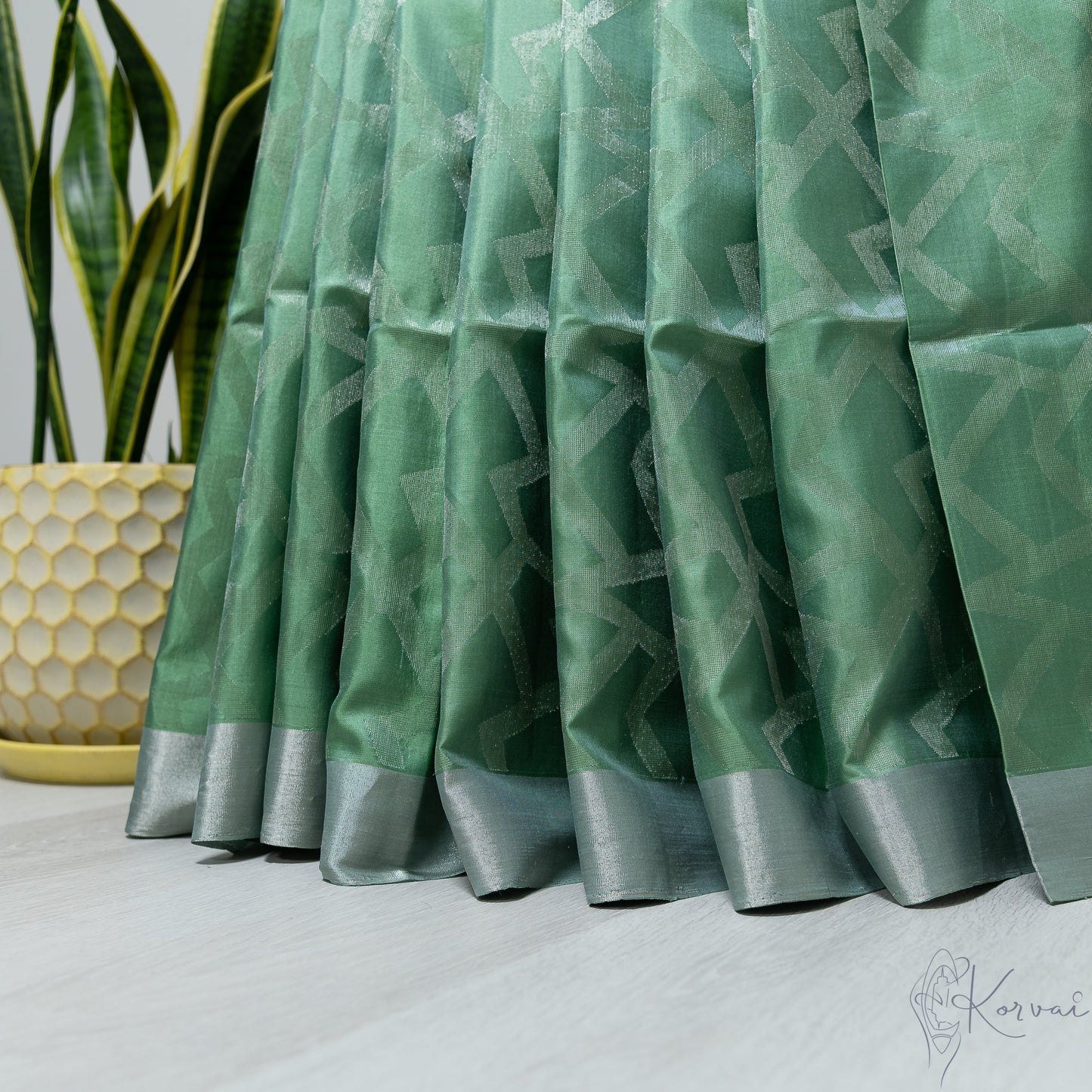 Pleated view of pastel green soft silk saree with silver geometric design.