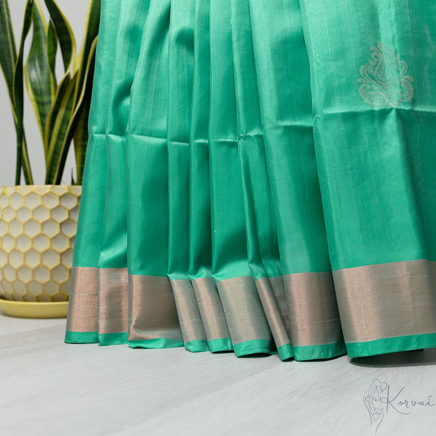 Pleated view of pastel green soft silk saree with copper zari border.