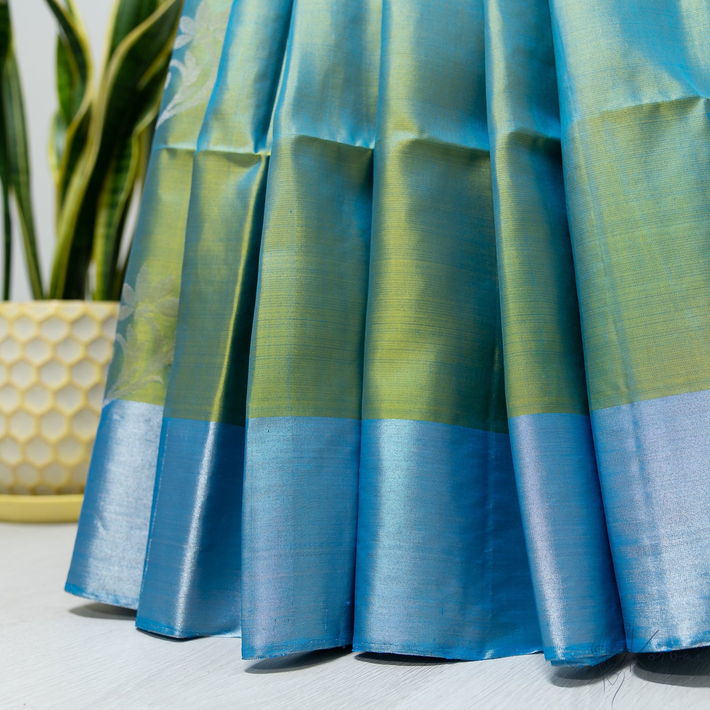 Pleated view of blue green soft silk saree with blue border.