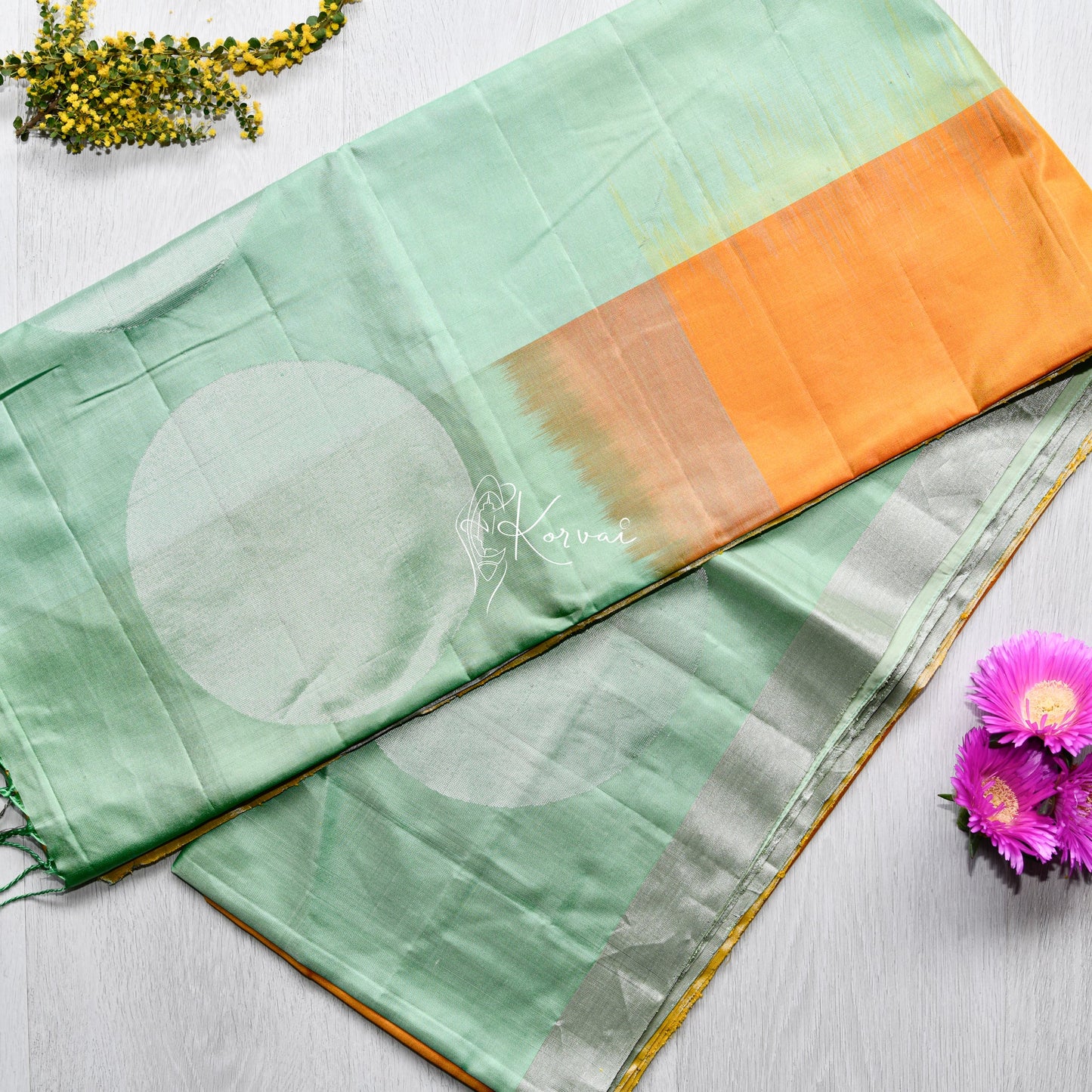 Top view of amber coloured soft silk saree with pastel green border and pallu featuring circle motifs.