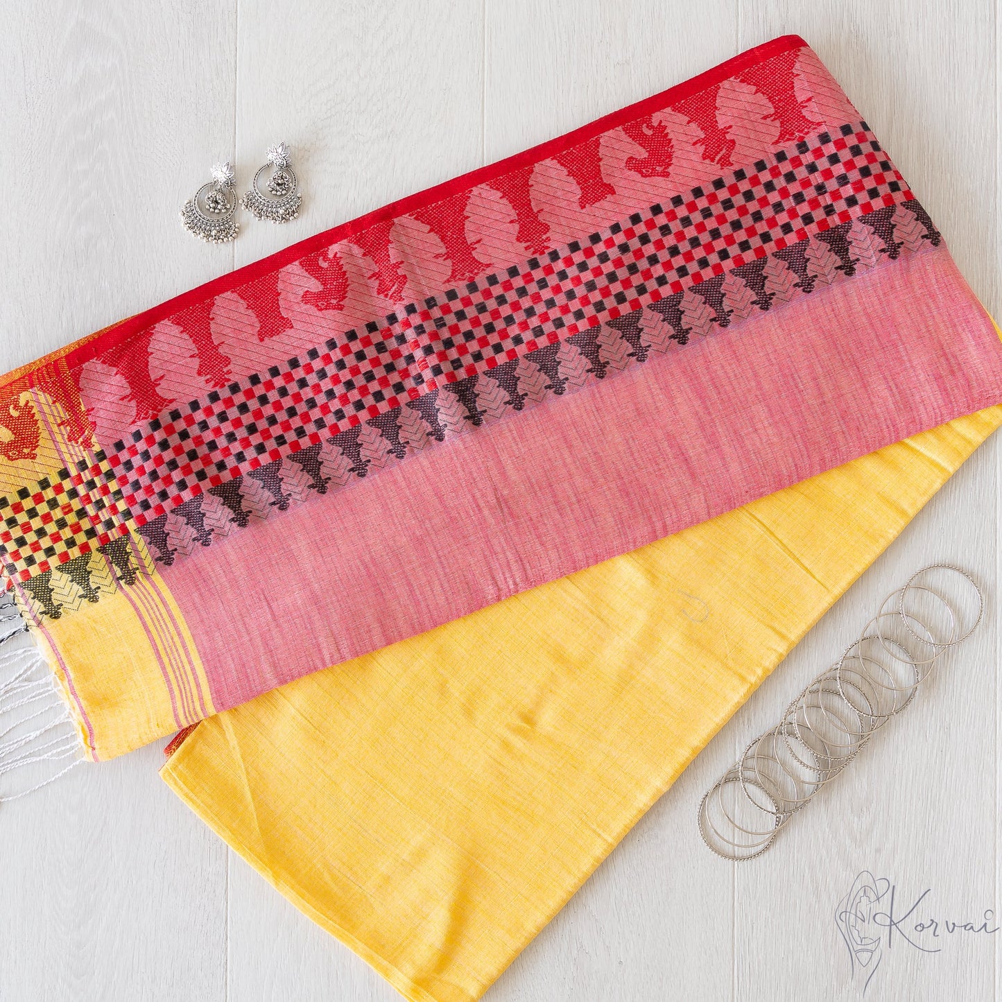 Picture showing a pleasant yellow coloured kadhi cotton saree folded in half with pallu facing up. The pallu has chess board and its coins as motifs along the border.