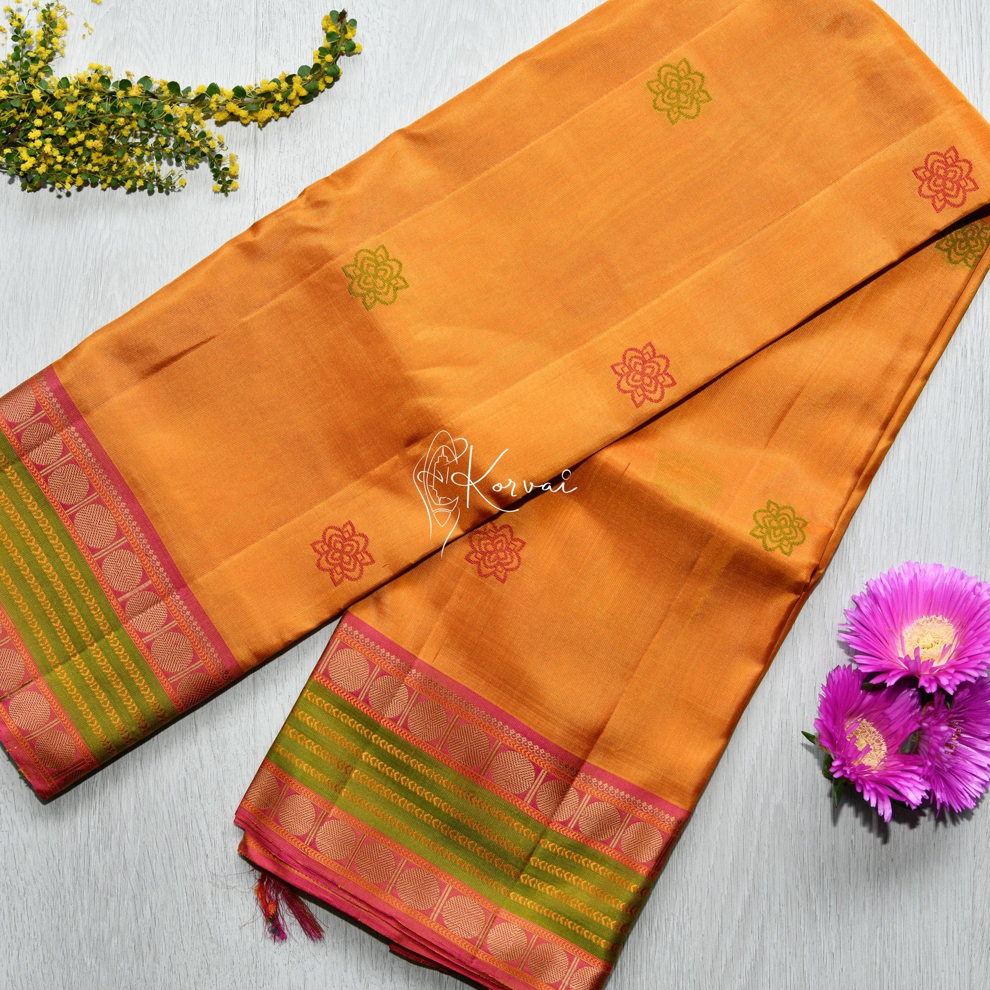 Top view of yellow soft silk saree with pink and green double border featuring flower motifs in pink and green.